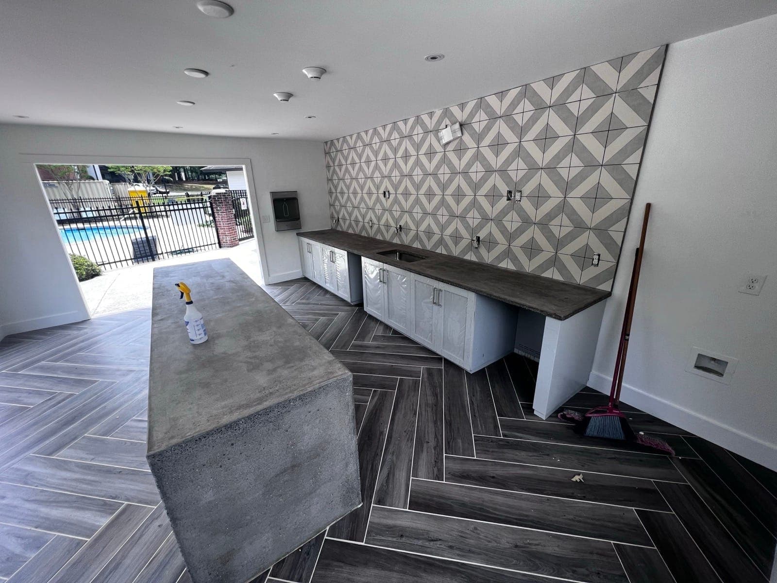 Built-in outdoor kitchen with concrete counters and a herringbone-tile wall, opening to the pool patio, Charlotte NC