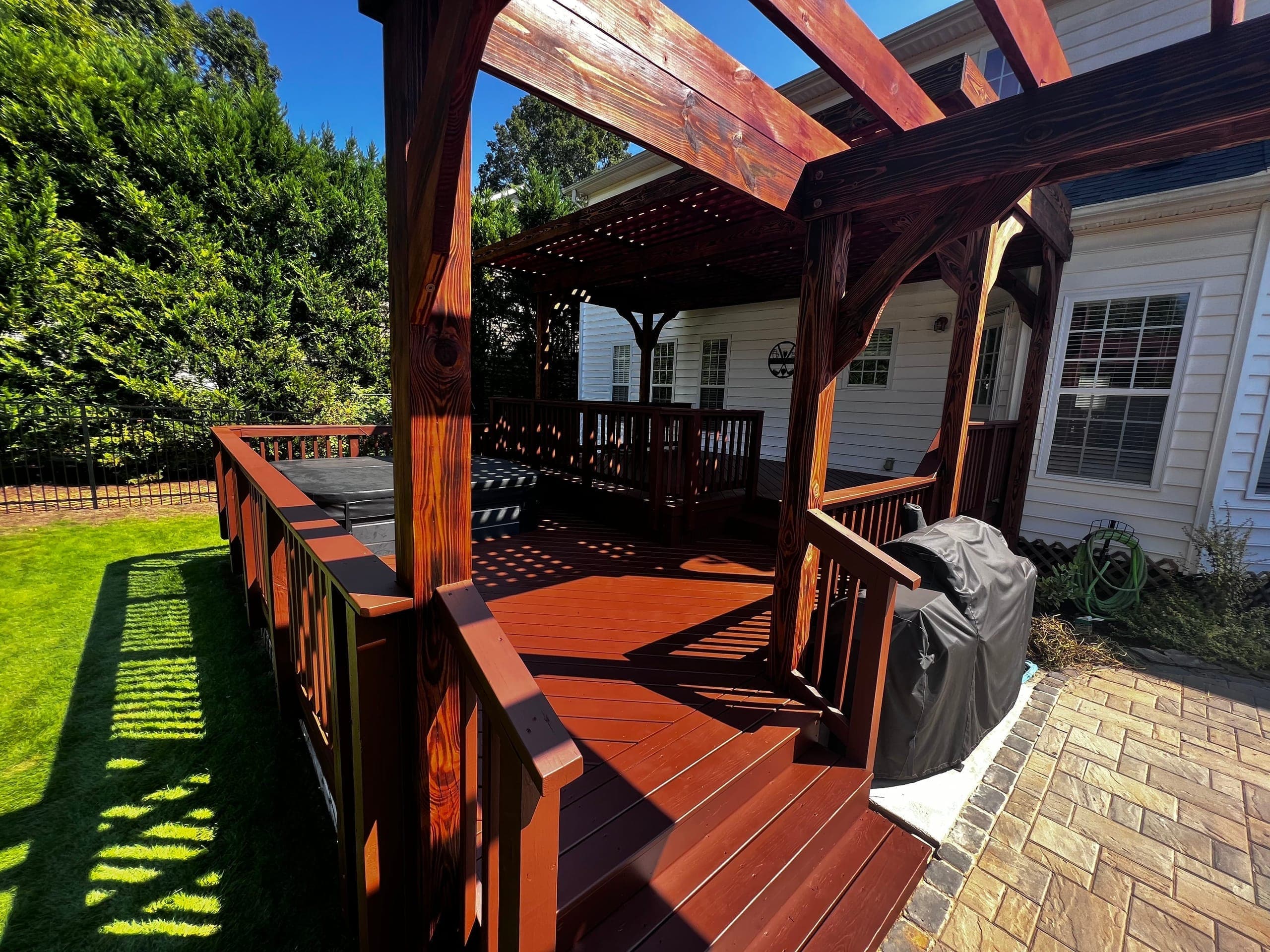 Dark-stained composite deck under a cedar pergola with a paver patio and grill, Charlotte NC