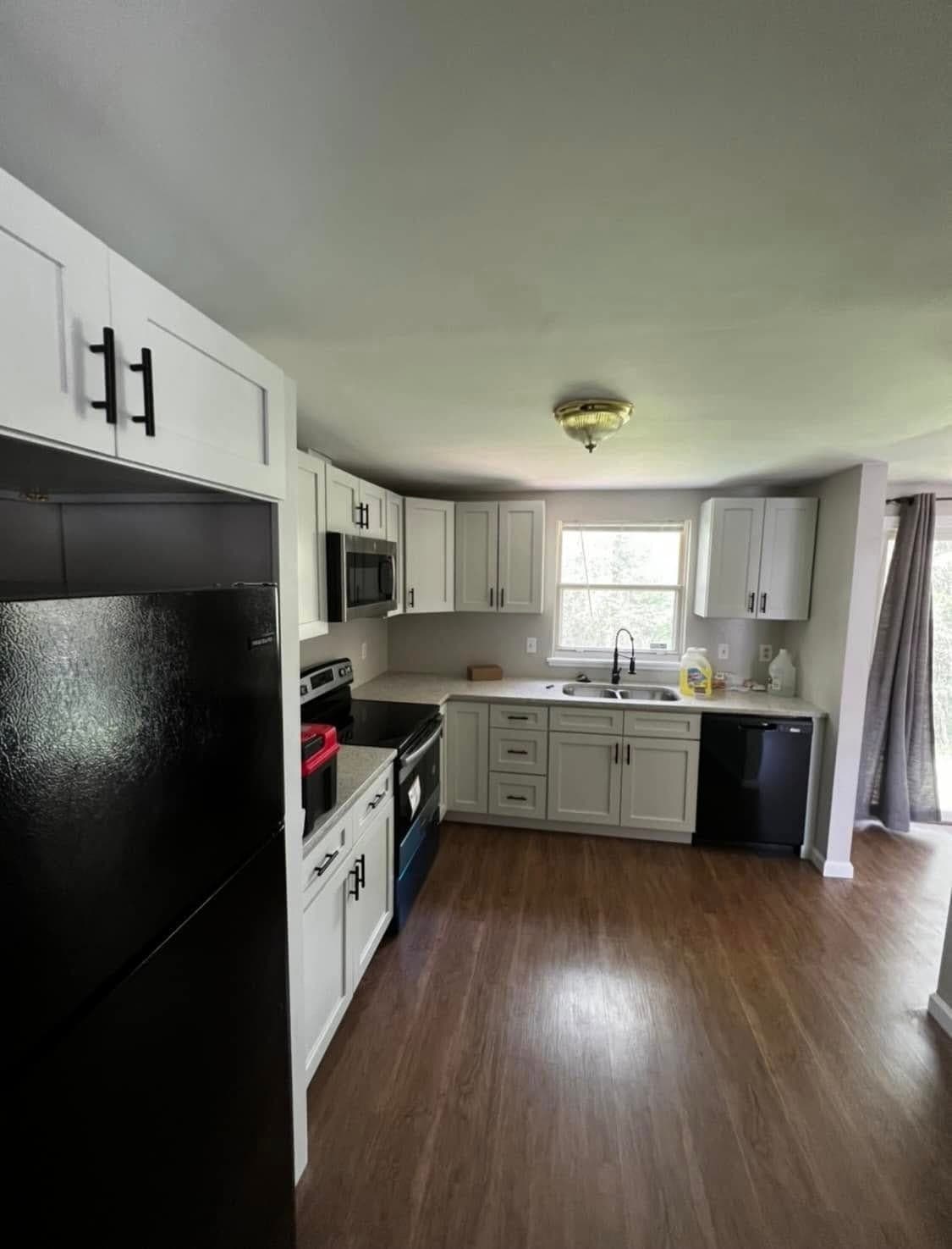 Remodeled white shaker kitchen with black hardware, speckled counters, and a wood-look floor opening to the living room, Charlotte NC